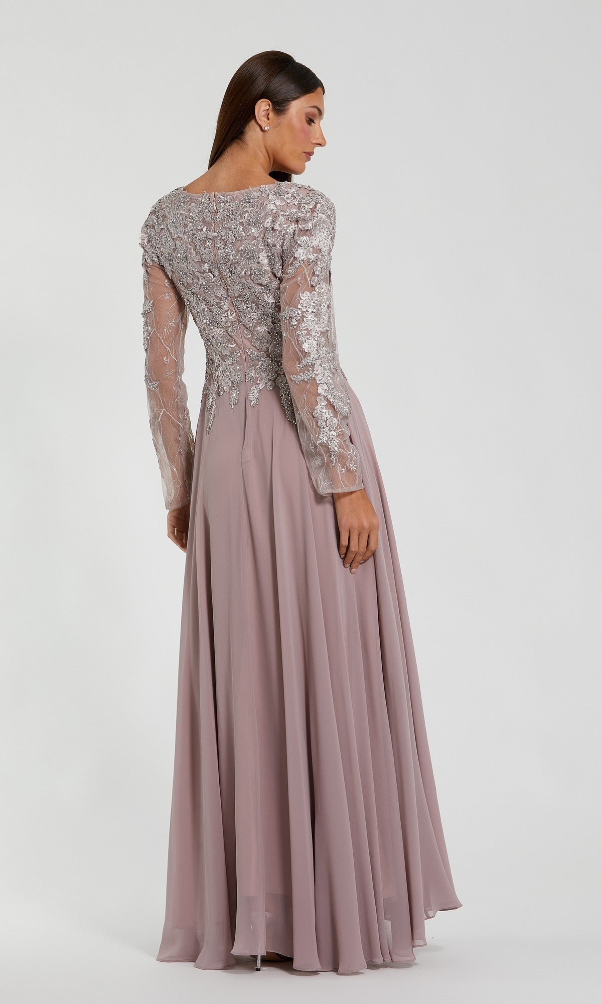 A woman faces away, wearing the Mac Duggal 20388 Long Sleeve Special Occasion Dress with chiffon fabric, sheer silver-embroidered lace sleeves and back, and a flowing mauve skirt.